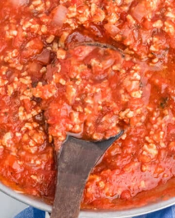Spaghetti sauce with ground beef in a skillet with a ladle.