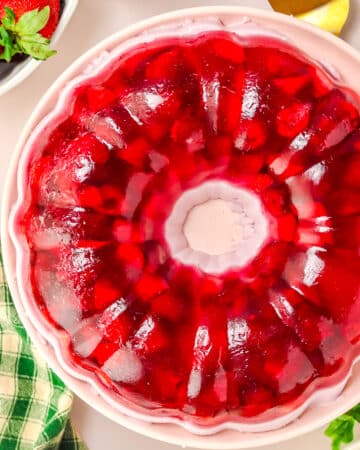 Strawberry jello mold on white serving plate.