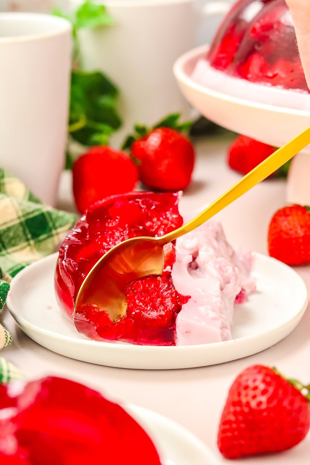 A slice of red jello with strawberries on a white plate with gold fork.