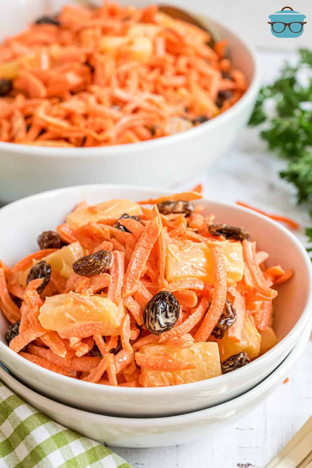 Two bowls of Carrot salad with raisins on a white counter top.
