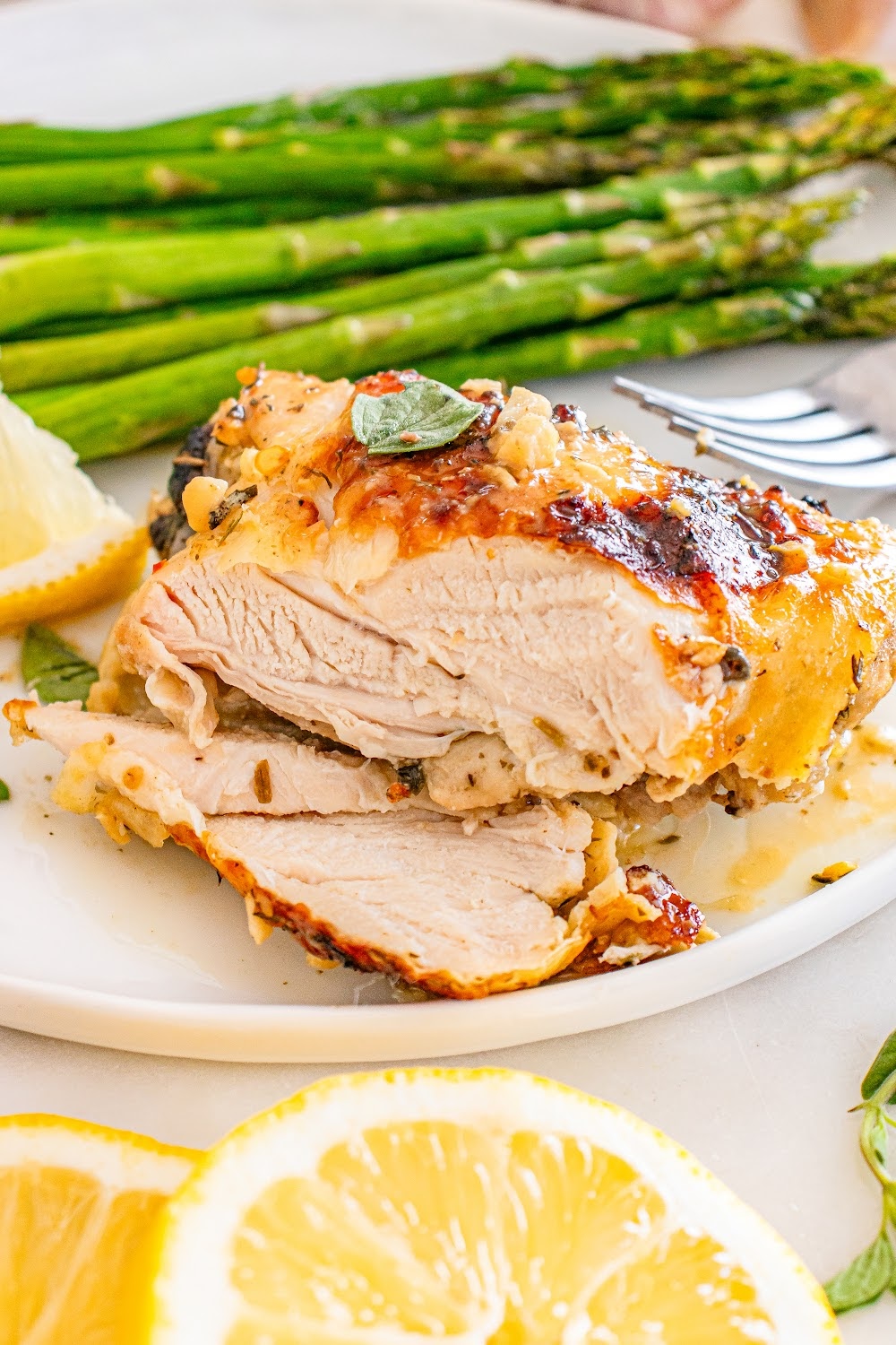 A chicken thigh sliced on a plate next to asparagus. 
