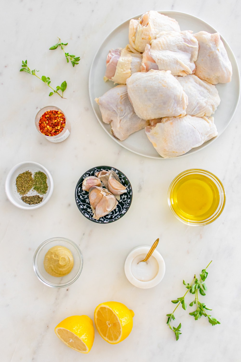 Greek Lemon Chicken Thighs Ingredients on a white marble countertop.