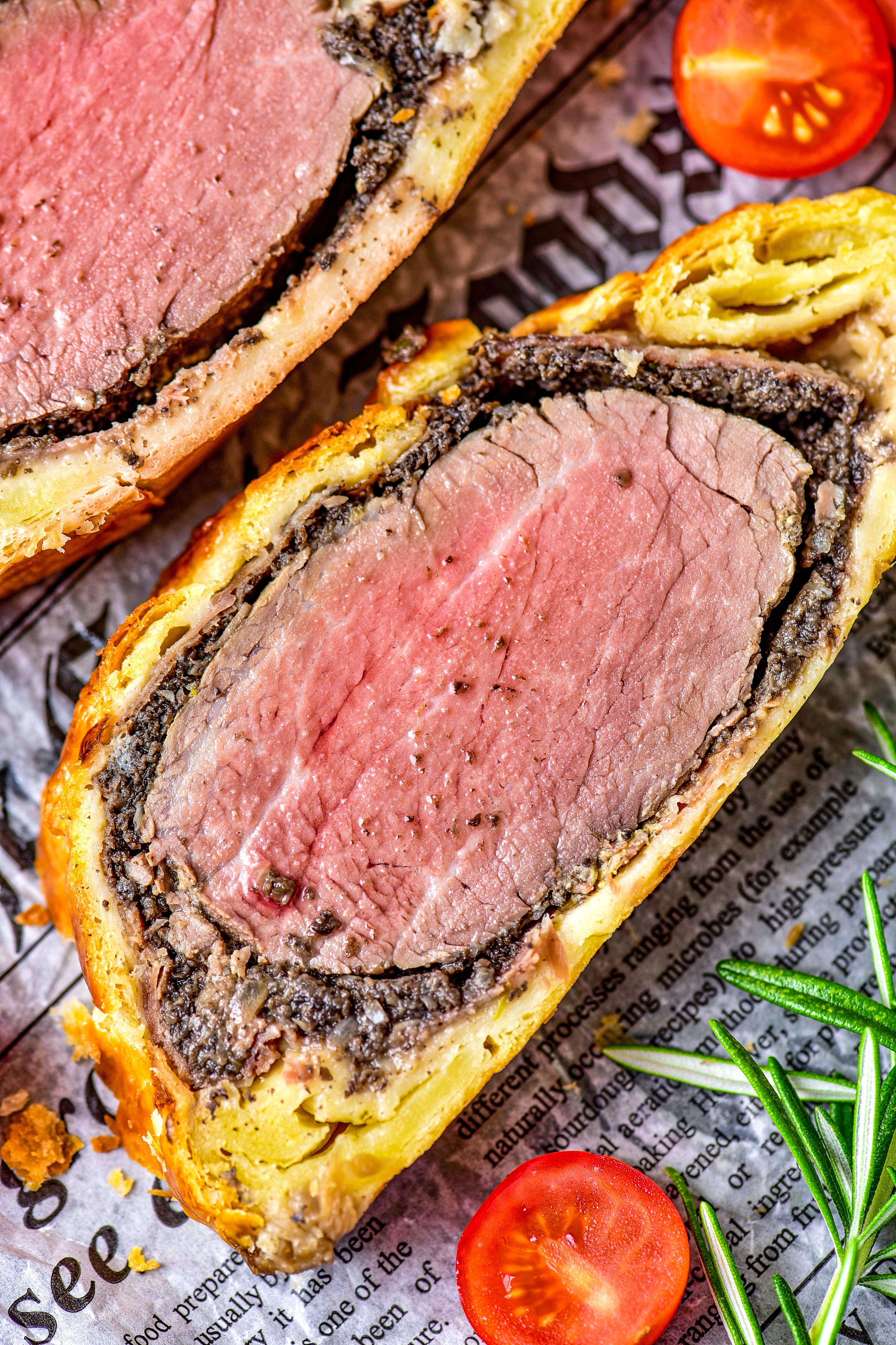 Two slices of Beef Wellington laying flat on a tray,