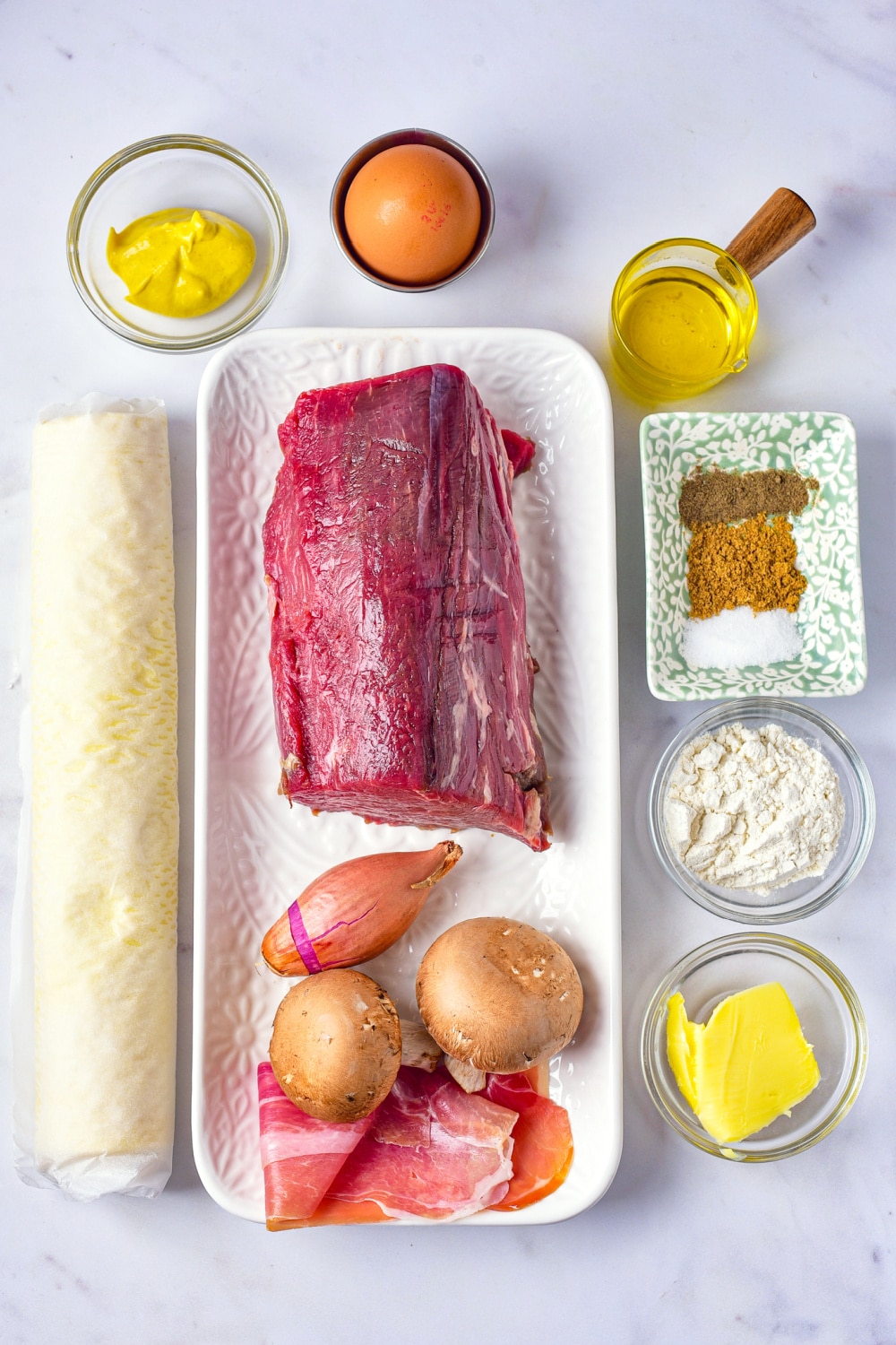 Ingredients needed to make Beef Wellington displayed on a white marble countertop.