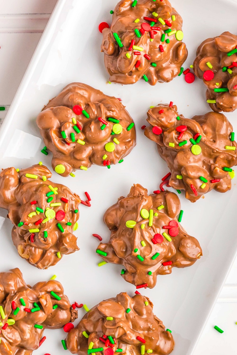 A white tray with chocolate candies topped with Christmas sprinkles.