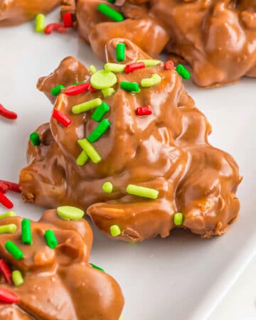 Red and green sprinkles top chocolate peanut candy string on a white plate.