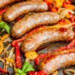 Cooked Italian sausages with bell peppers and onions on a sheet pan.