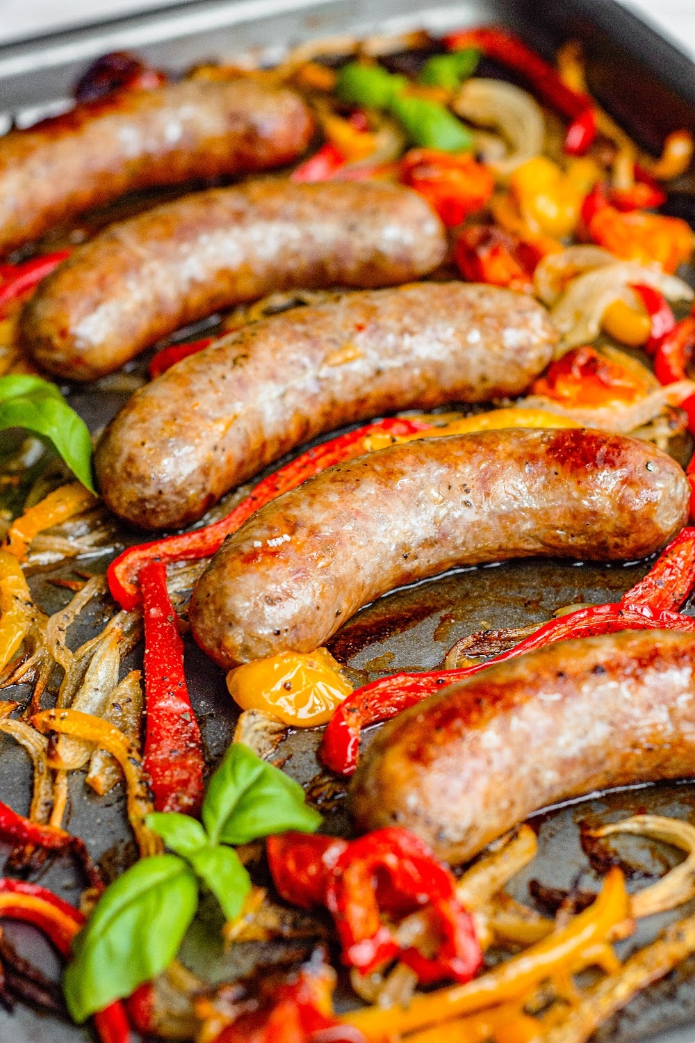 Cooked Italian sausages with bell peppers and onions on a sheet pan.