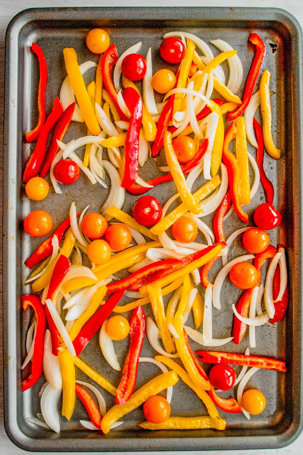 Cherry tomatoes, sliced bell peppers and onions on a sheet pan.