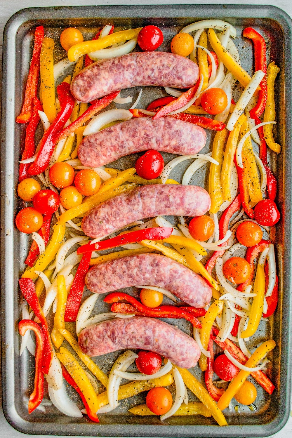 Uncooked Italian Sausages in a bed of sliced onions and peppers. 