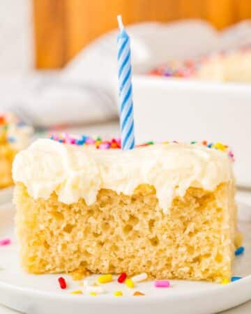 A piece of homemade vanilla sheet cake on dessert plate topped with a birthday candle.