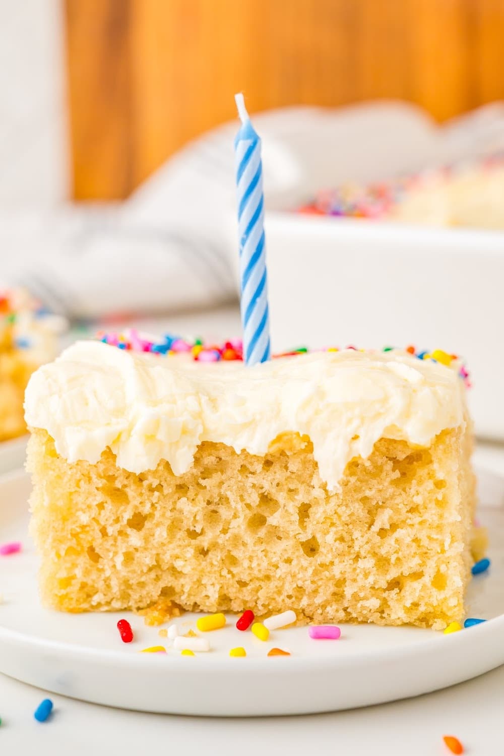 A piece of homemade vanilla sheet cake on dessert plate topped with a birthday candle.