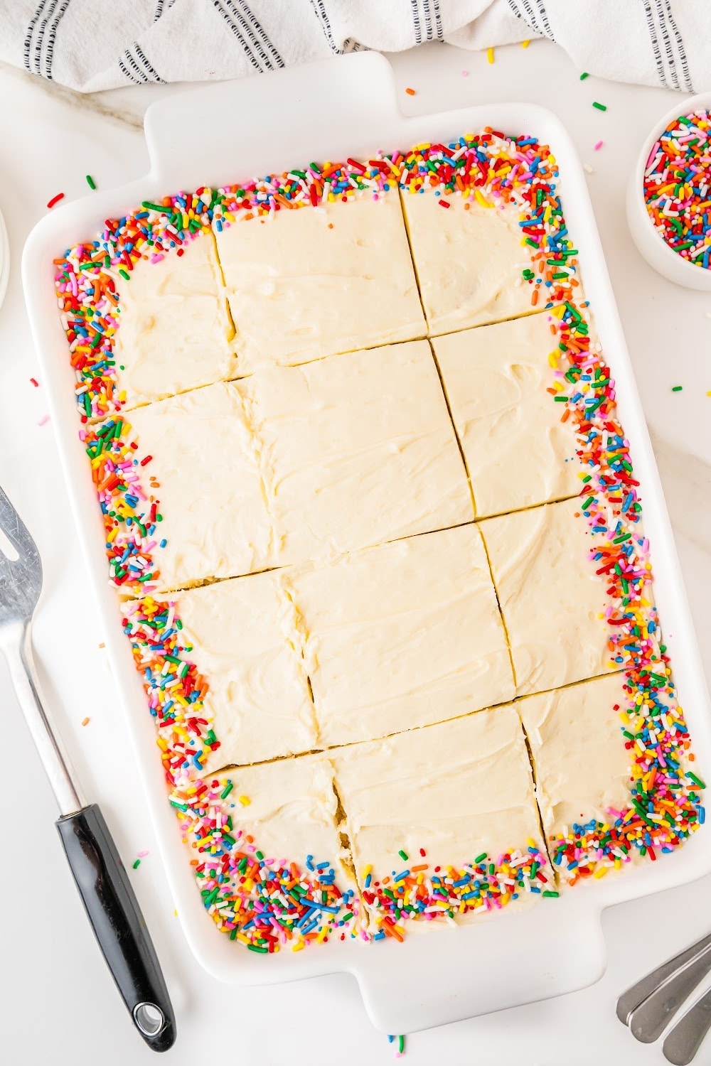 Homemade vanilla birthday cake with colorful sprinkles sliced in squares in a 9x13 baking dish.