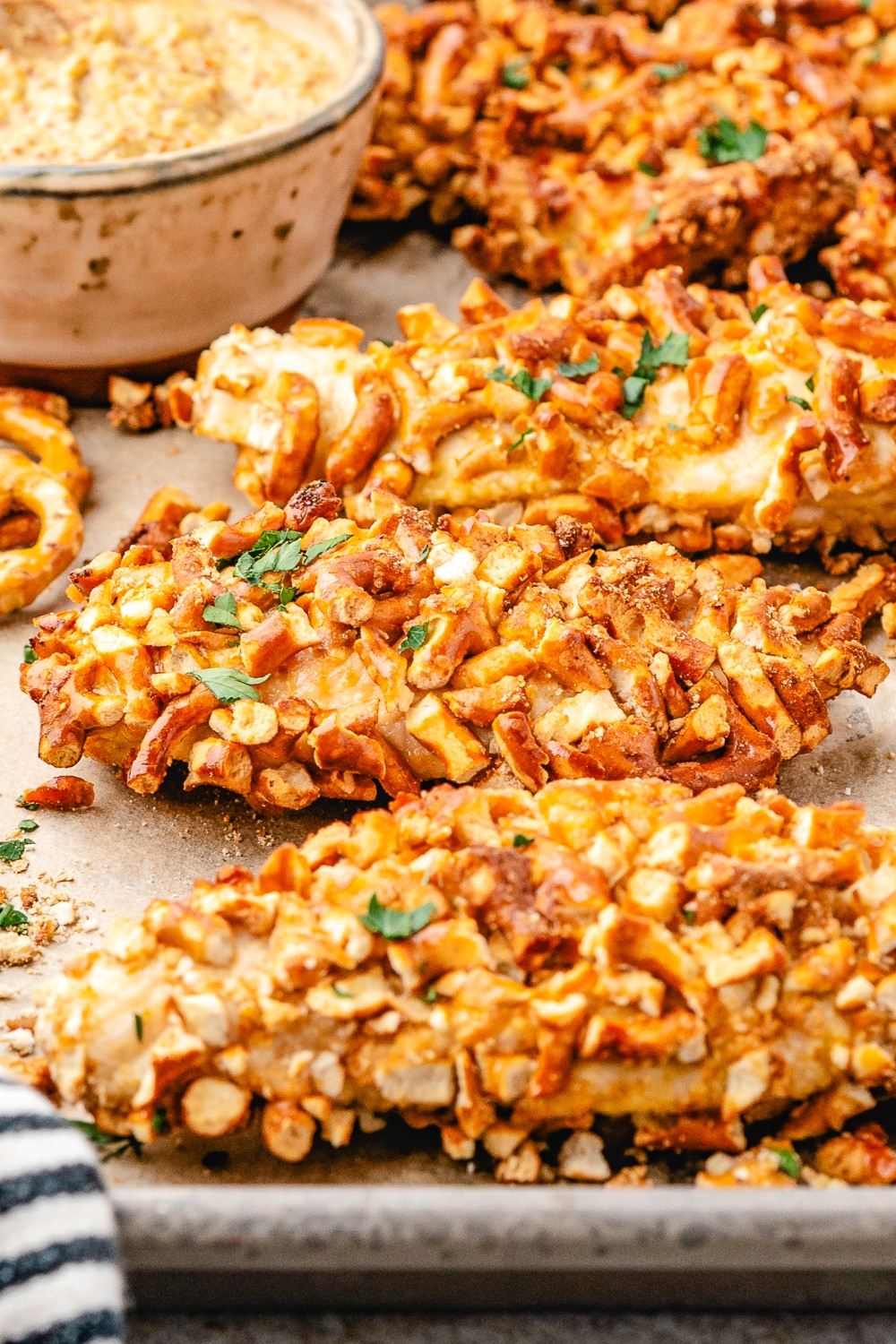 Three chicken strips with with crushed pretzel coating on a baking tray.