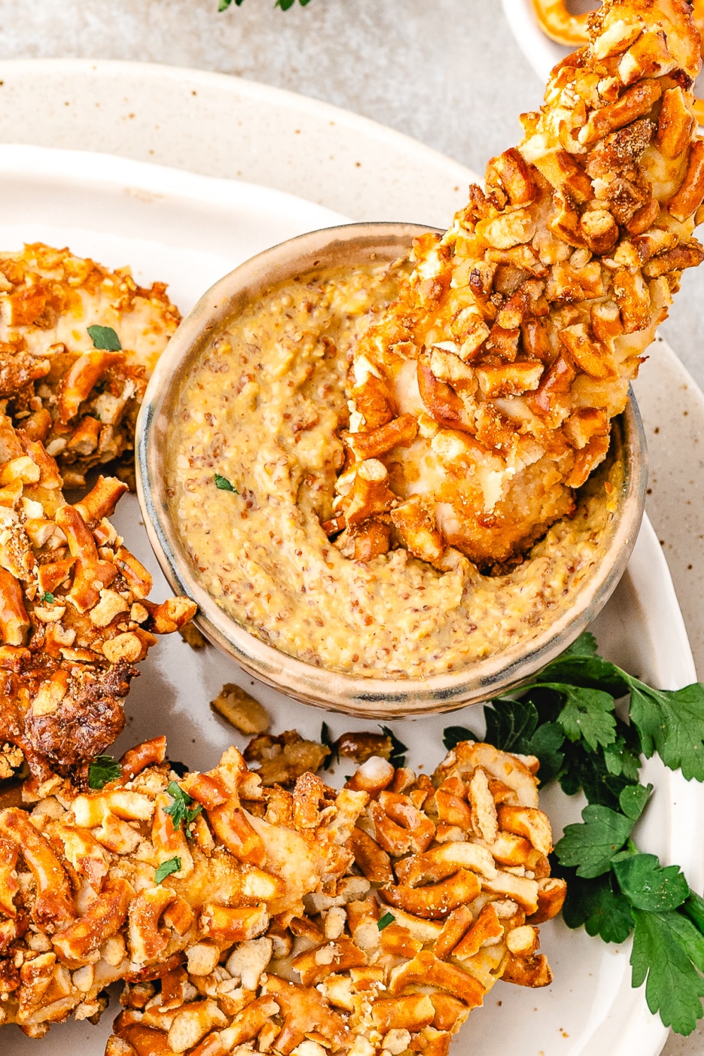 Chicken strip coated in crushed pretzels being dipped in a creamy honey mustard sauce. 