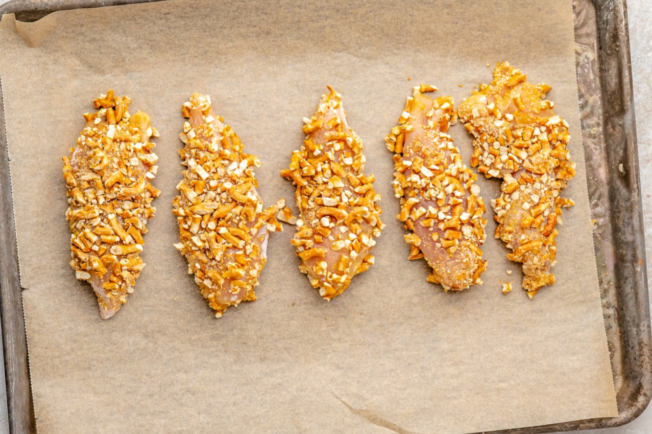 Pretzel Crusted Chicken on a parchment lined baking sheet before being baked. 